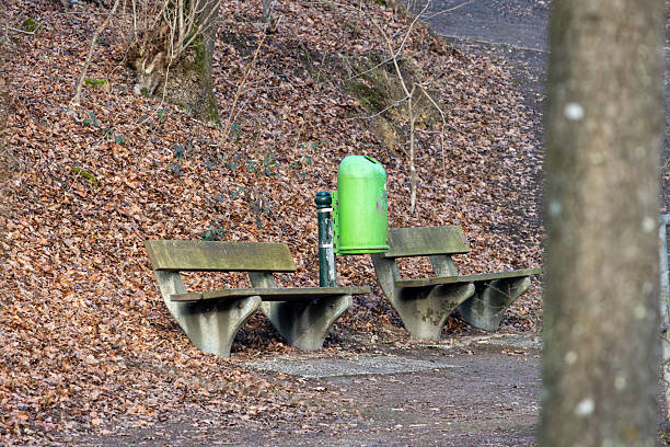 A green trash can sits on a bench in a park
