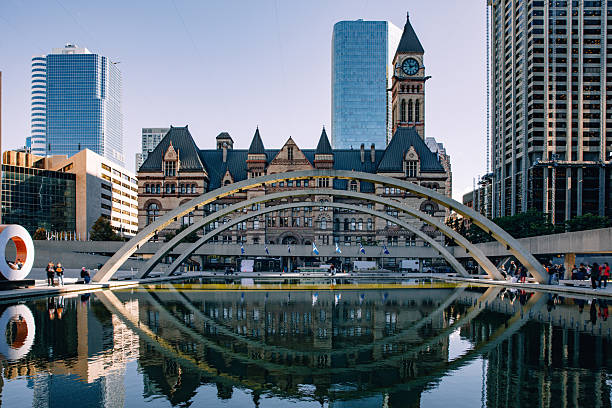 Reflection of Toronto City Hall and Nathan Phillips Square arch in calm water, surrounded by modern downtown buildings. The composition emphasizes symmetry, civic architecture and the blend of historic and contemporary design.