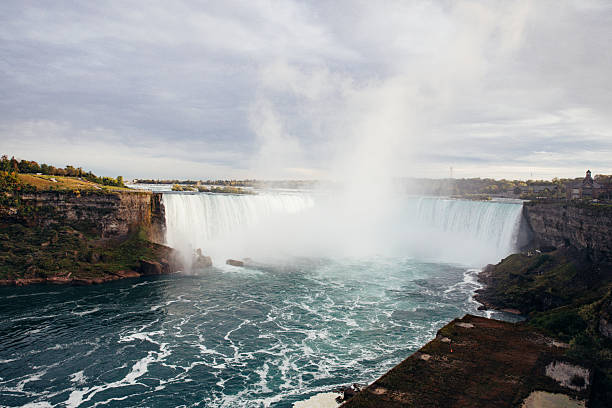 Wide view of Niagara Falls with massive volumes of water cascading over the edge into the river below. Natural power, mist and movement illustrate one of North America’s most famous natural landmarks.