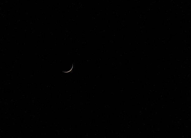 A crescent moon hangs in the night sky. Stars are visible around it, creating a clear view of the lunar phase. The scene shows darkness stretching across the horizon.