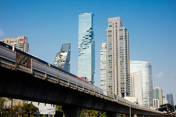 Futuristic Maha Nakhon tower in Bangkok skyline from N Sathon Road with BTS skytrain in foreground