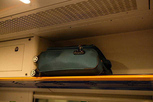 Suitcase stored on overhead luggage shelf inside modern passenger train. Travel baggage secured above seats in railway carriage interior. Public transport, travel and commuting concept.