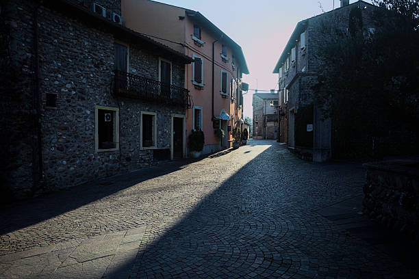 Cobbled street between buildings with facades in the shade and sunlight filtering through the buildings illuminating part of the street