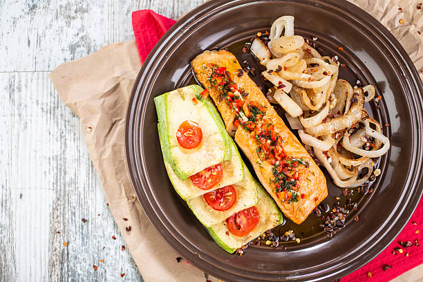 A plate with grilled salmon fillet seasoned with dill and paprika sauce, served with grilled zucchini with tomato rings and fried onions.