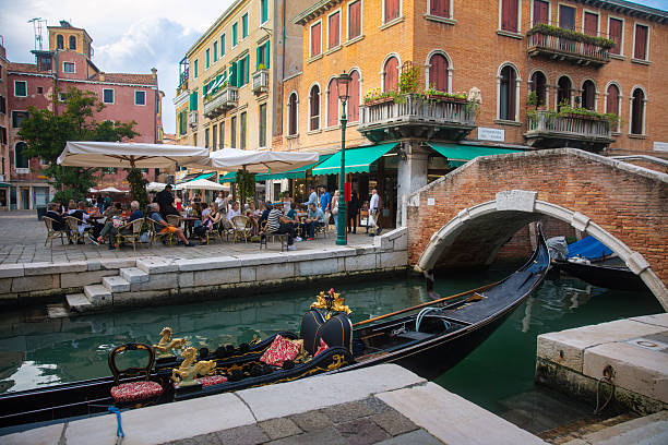 Authentic view of a Venetian canal featuring a traditional gondola, historic brick buildings, and a small pedestrian bridge. The scene captures the timeless beauty and everyday atmosphere of Venice, highlighting its architectural heritage, calm waterways, and lived-in urban character beyond iconic landmarks.