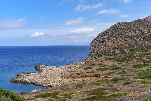 A picturesque view of Puntazza A Carcara, a beautiful, secluded cove on Levanzo Island, featuring vibrant turquoise and deep blue Mediterranean water gently meeting a rocky beach, ideal for themes of pristine travel and quiet escape.