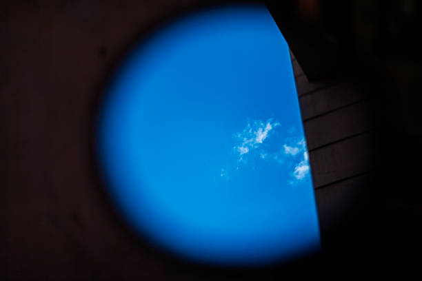 Vibrant blue sky with scattered white clouds reflected in a scooter's circular rear-view mirror, observed in Seville, Andalusia, Spain.