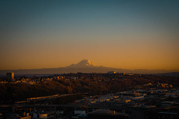 Cinematic wide-angle view of the Seattle skyline at sunset, featuring the snow-capped peak of Mount Rainier glowing in the distance.