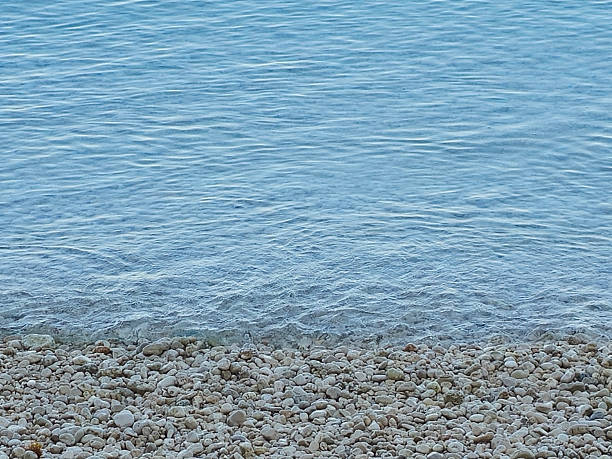 Calm sea meeting a pebble-covered shore. Natural coastal scene ideal for travel, vacation, summer, relaxation, and seaside background concepts