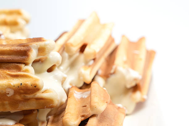 Stacked waffles filled with creamy sauce fading into soft focus. Minimal dessert composition with shallow depth of field on white.