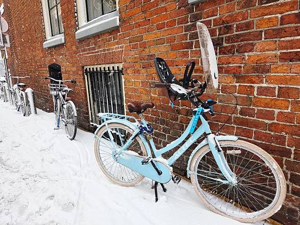 GRONINGEN, NETHERLANDS - JANUARY 07, 2026: A blue Altec bicycle equipped with a child seat and a plastic windshield is parked against a red brick wall on a sidewalk covered in deep snow during a winter storm