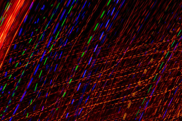 Bright light trails and spots create futuristic patterns against a dark backdrop. Abstract background with defocused lines and spots, made by glowing fiber optic lights.
