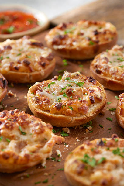 Pepperoni pizza bagel bites topped with melted cheese and herbs, arranged on a wooden board. A classic baked appetizer inspired by pizza flavors, styled for casual entertaining and snack food concepts.