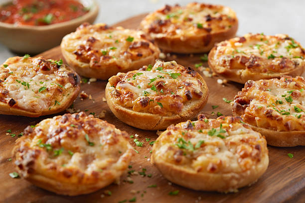 Pepperoni pizza bagel bites topped with melted cheese and herbs, arranged on a wooden board. A classic baked appetizer inspired by pizza flavors, styled for casual entertaining and snack food concepts.