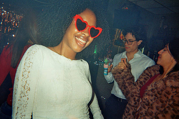 Young diverse adults laughing and dancing at a retro-themed nightlife party with a bubble gun, heart sunglasses and film-grain vibe, carefree friends enjoying good times