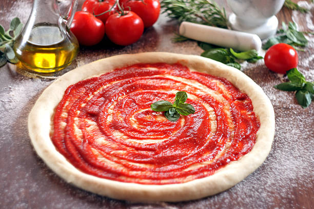 Raw pizza dough with tomato sauce and basil leaves. Selective focus