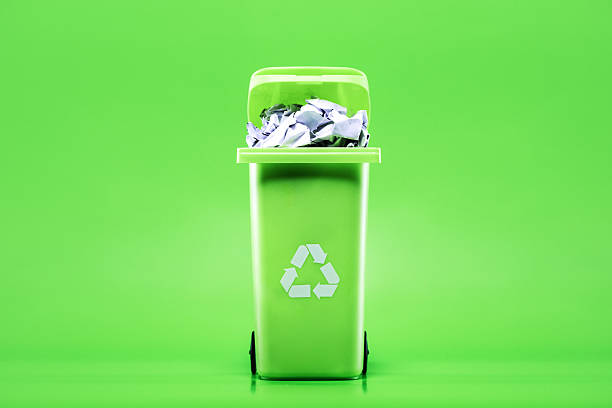 A recyclable waste rubbish bin on green studio background, filled with crumpled up paper.  Environment friendly concept.