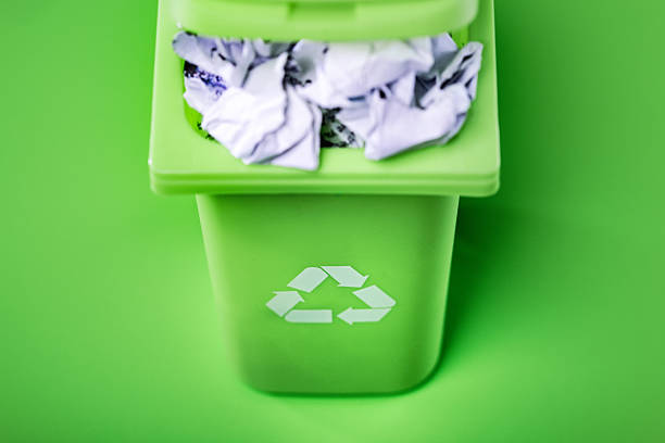 A recyclable waste rubbish bin on green studio background, filled with crumpled up paper.  Environment friendly concept.