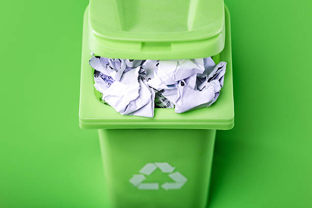 A recyclable waste rubbish bin on green studio background, filled with crumpled up paper.  Environment friendly concept.