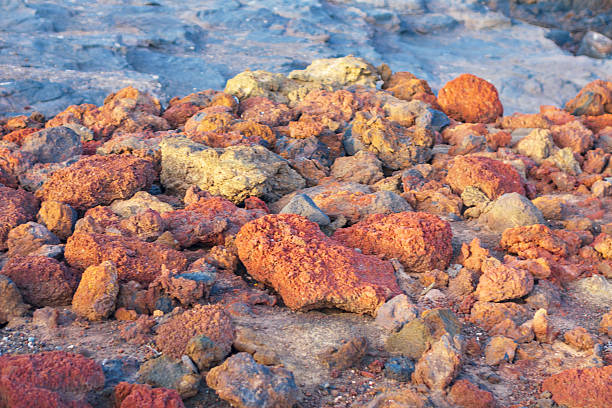 Reddish scoria rocks, type of porous volcanic rock. The varied textures and hues suggest an active, natural volcanic environment