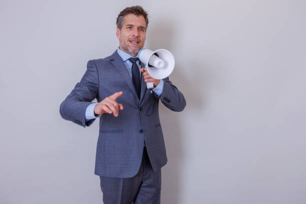 Adult businessman in a suit holding a megaphone and actively communicating, making an important announcement or sharing information