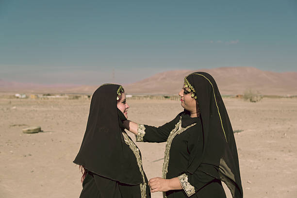 Two young women of Middle Eastern descent spend time together in the desert, sharing a joyful and peaceful moment under the warm sun.