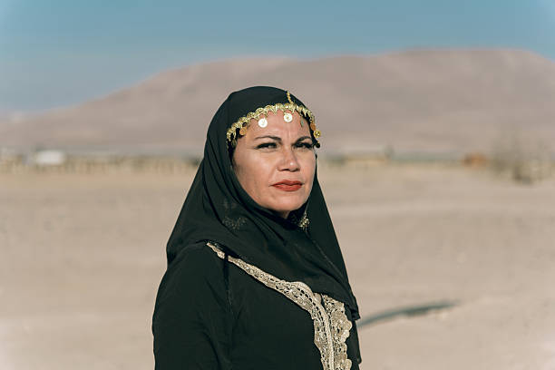 A young Middle Eastern woman without a face covering looks serious and composed while standing alone in the desert.