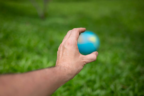 Human hand extended toward a blurred globe resting on green grass, using selective focus to emphasize the abstract concept of global responsibility, environmental fragility, and the future of the planet. Conceptual image representing sustainability, climate change awareness, environmental protection, and care for Earth, with ample copy space.