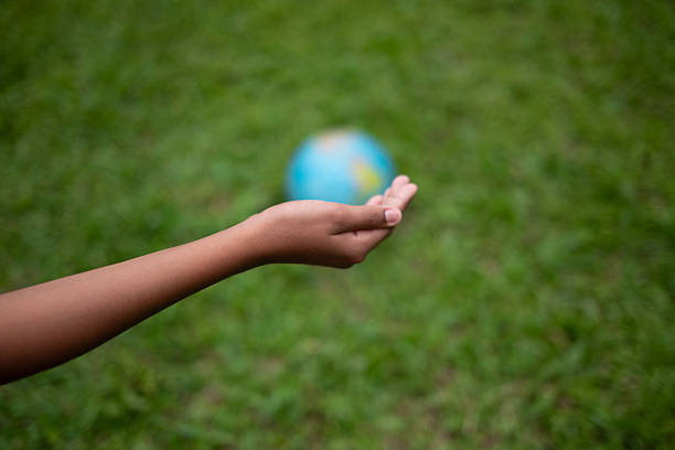 Young boy's hand holding planet Earth globe at natural park background as Earth day to save this planet with ESG principle and environment friendly energy for brighter future. Gyre