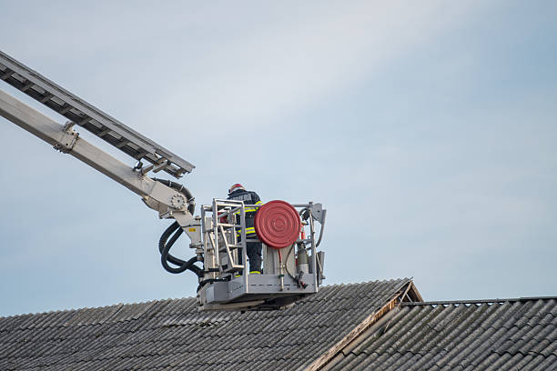 Firefighters in elevated platform extinguish burning house using extended ladder equipped with water hose to spray water onto the building roof with smoke. Fireman extinguishing fire in the city.
