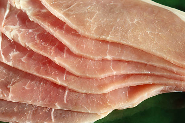 Stock photo shows thin slices of raw cured bacon showcasing both lean and fat layers, processed with nitrites for preservation. Arranged for cooking or butcher display, highlighting traditional charcuterie and fresh pork preparation