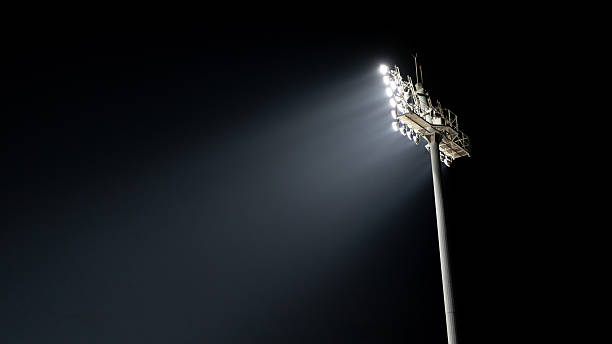 Professional stadium sports lighting on a tall pole glowing against a black background. Ideal for sports, arena, and competition concepts.