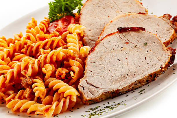 Roast pork loin cutlets with tomato pasta on white background