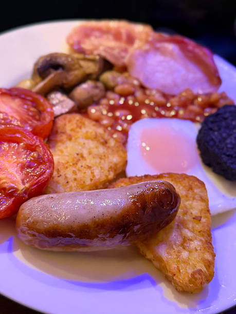 Image of full English fried breakfast with sausage, egg, baked beans, hashbrown, tomato, and mushrooms, hearty British morning meal