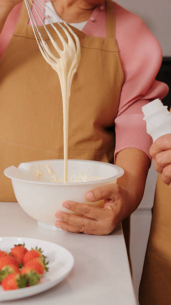 Senior couple preparing dessert by cracking eggs, pouring milk, and mixing ingredients together