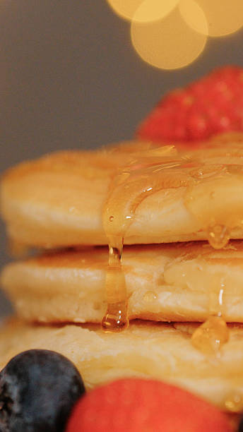 Drizzling honey over pancakes topped with strawberries and berries