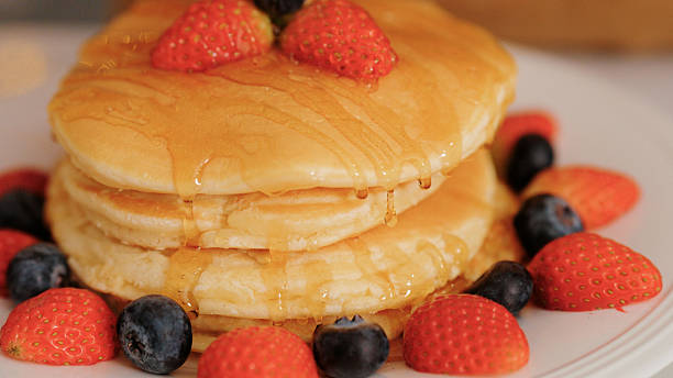 Drizzling honey over pancakes topped with strawberries and berries