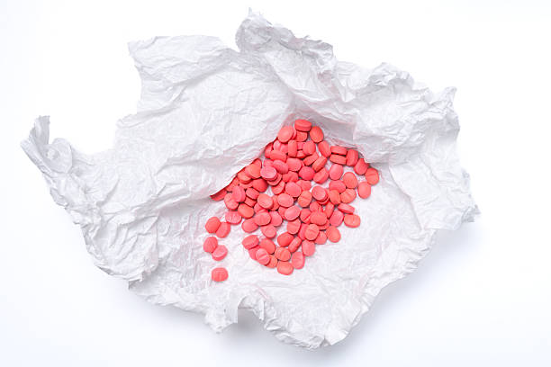 Numerous pink tablets scattered across crumpled white paper. Striking composition on a light background, emphasizing medicine, pharmaceuticals, and health themes.