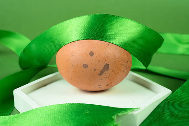 Chicken eggs on white podium with green ribbon on green background.