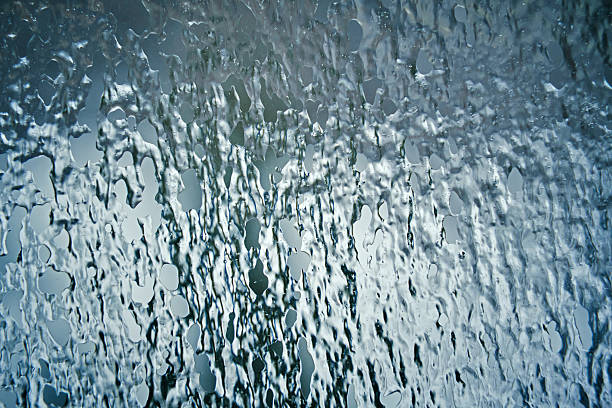 A close-up, abstract photograph showing intricate frost patterns, ice crystals, and frozen water droplets on a glass surface. The cool blue and grey tones create a wintry, textured background. Ideal for seasonal backgrounds or nature-themed designs
