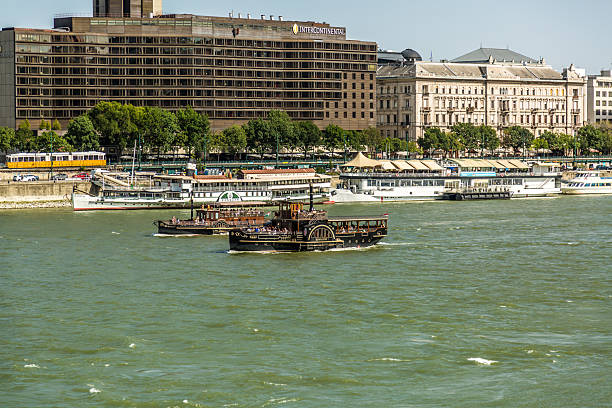 Budapest, Hungary – August 28, 2025. Tourist cruise ship sailing along the Danube River with city buildings and riverside infrastructure in the background, capturing river tourism and daily life on the water.
