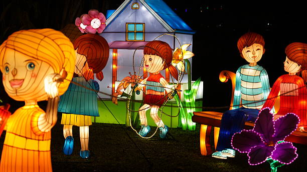 A captivating night scene featuring a whimsical lantern festival. Illuminated figures of children, a charming house, and vibrant flowers glow, creating a magical atmosphere. Perfect for themes of celebration, culture, and childhood wonder.