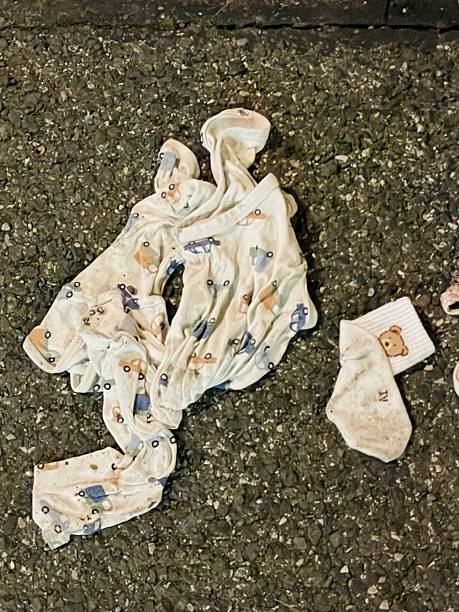 patterned blanket and sock on asphalt, crumpled beside single sock, damp texture under streetlight, urban roadside scene Taken on mobile device.
