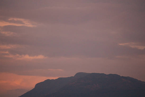 Sunset landscape with the sun disappearing behind hills and mountains under a dramatic sky. Warm evening light creates a calm and atmospheric scene inspired by nature, travel and reflection.