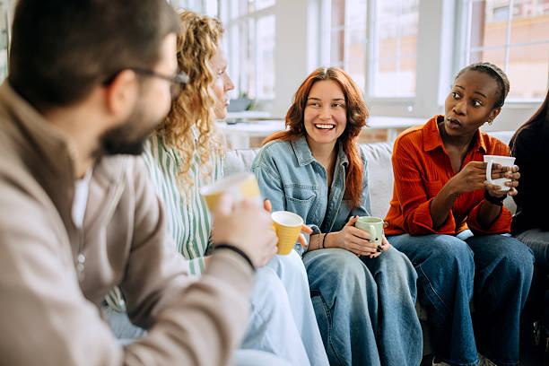A group of adults sits together in a modern office. They are engaged in conversation, sharing ideas while enjoying coffee. The atmosphere shows teamwork and collaboration.