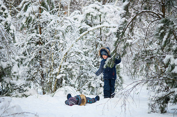Two young children enjoying active winter day outdoors in snowy forest. Kids play, explore nature, ride a sled, and have fun among snow-covered trees