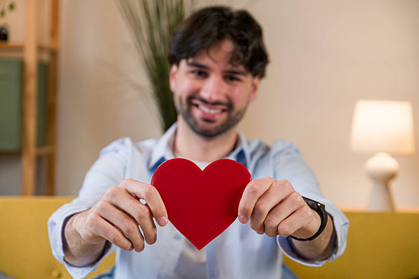 Young man smiling and extending a red heart towards the viewer