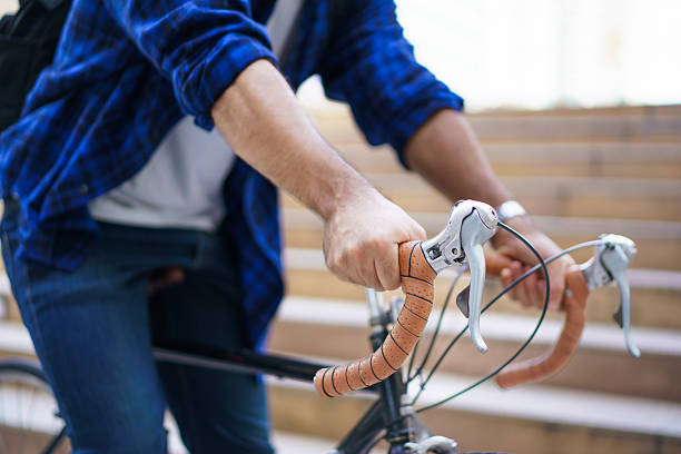 Close up of man holding bicycle handlebars in modern city. Urban cycling and commuting concept with copy space. Mobility, fitness, sustainable transportation lifestyle.