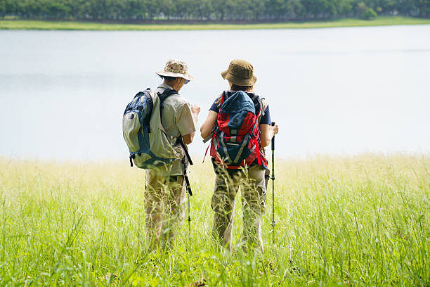 Two hikers with backpacks stand by a lake, taking a break and checking their route during an outdoor trip. They enjoy the peaceful scenery and fresh air while exploring nature as part of an active travel lifestyle.