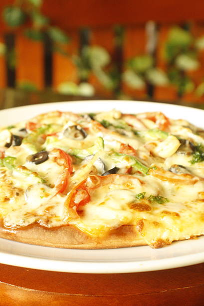 Delicious pizza topped with melted mozzarella cheese, sliced tomatoes, green bell peppers, and black olives, served on a white plate